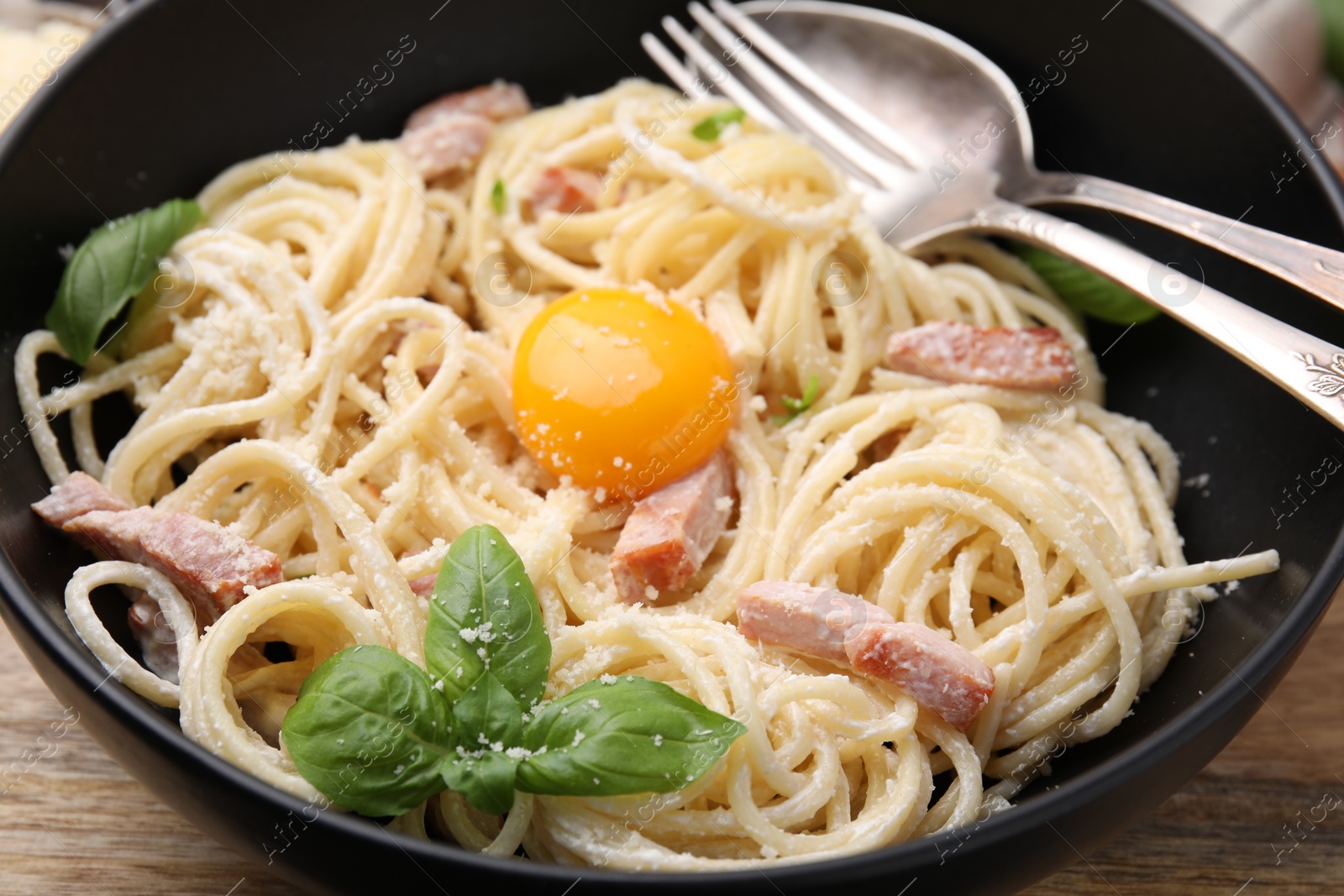 Photo of Bowl of delicious pasta Carbonara with egg yolk and cutlery on table, closeup