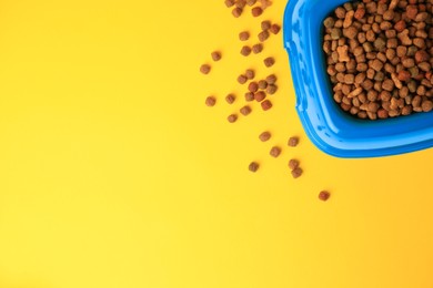 Photo of Dry pet food in feeding bowl on yellow background, flat lay. Space for text