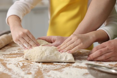 Making bread. Mother and her daughter kneading dough at wooden table in kitchen, closeup