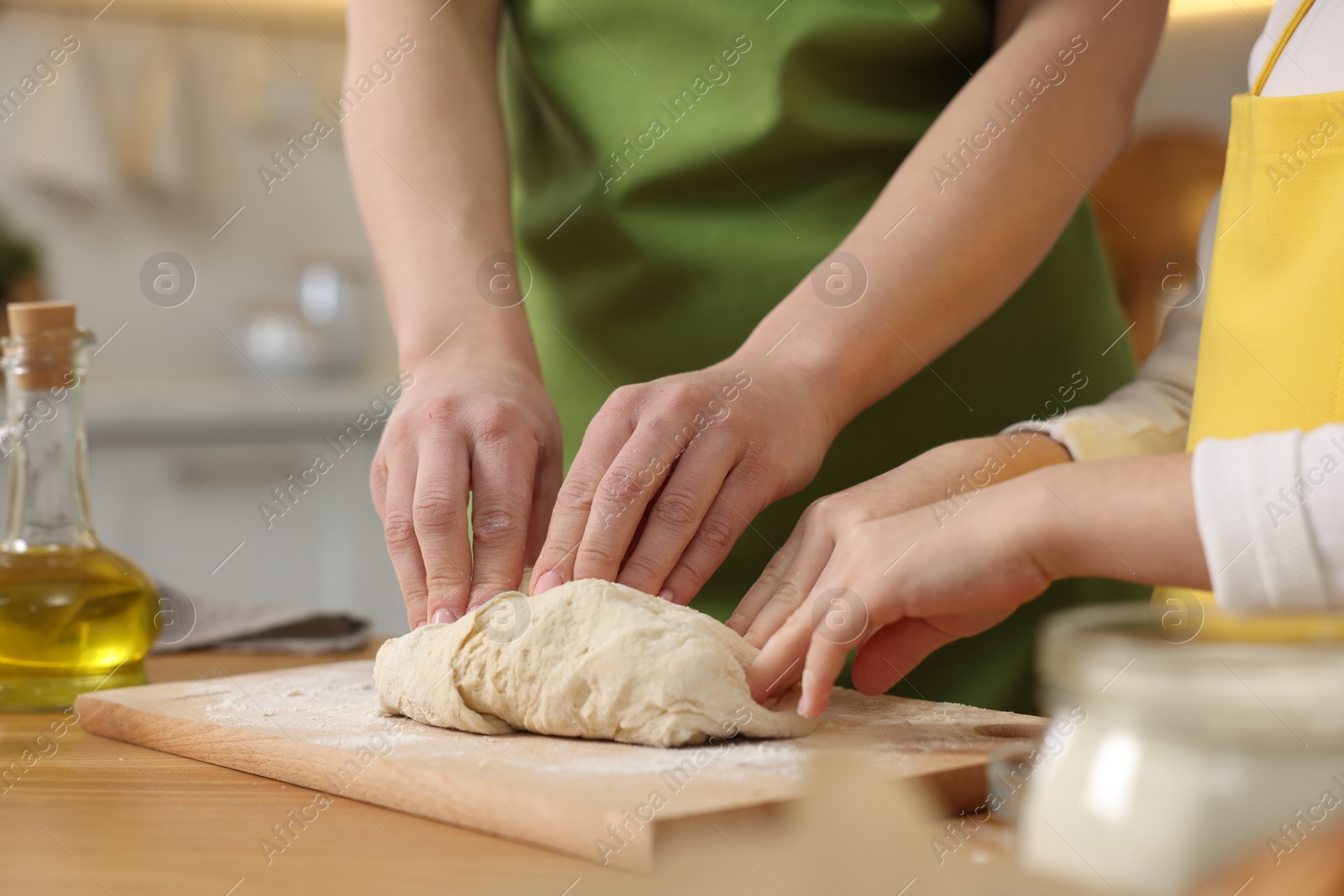 Photo of Making bread. Mother and her daughter kneading dough at wooden table in kitchen, closeup