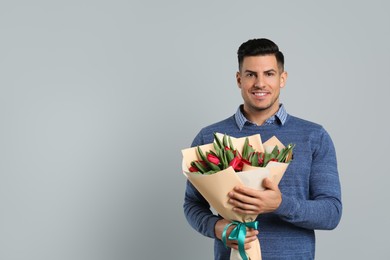 Happy man with red tulip flowers bouquet on light grey background, space for text. 8th of March celebration