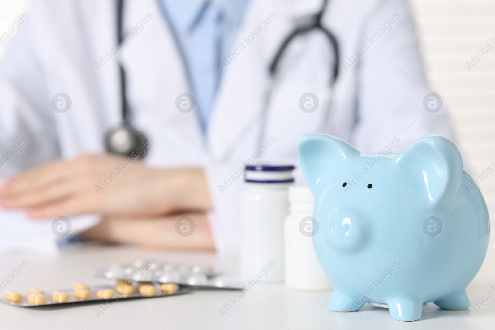 Photo of Doctor with piggy bank and pills at white table, closeup