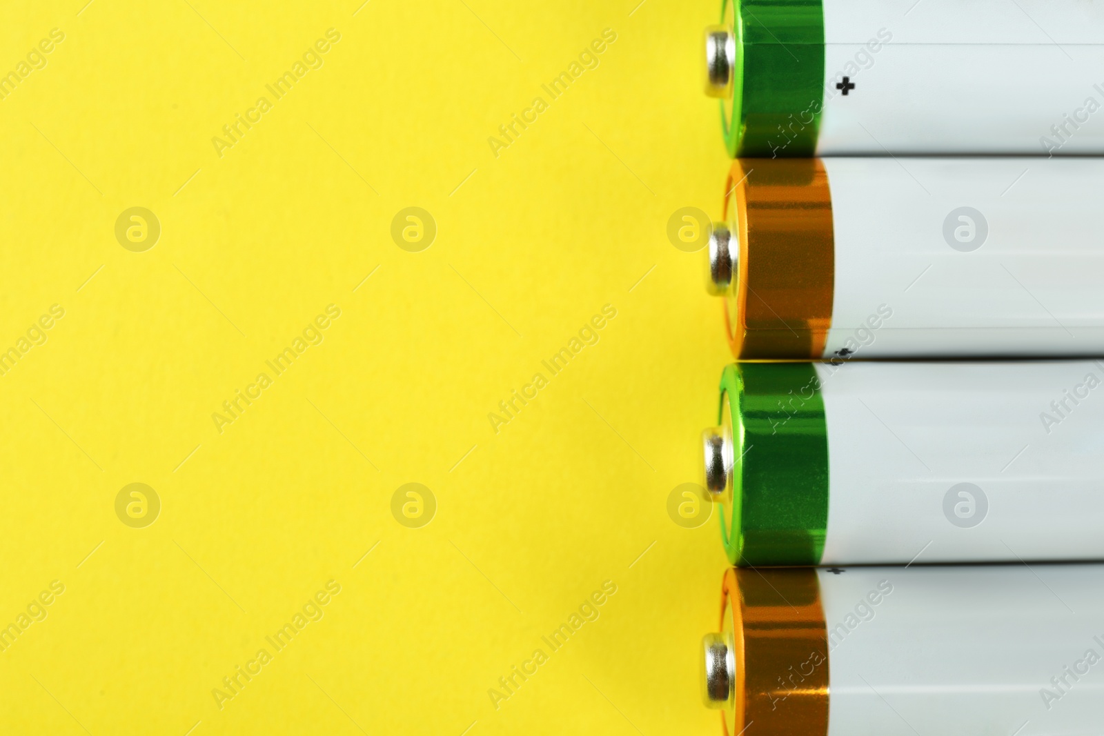 Image of New AA batteries on yellow background, flat lay. Space for text