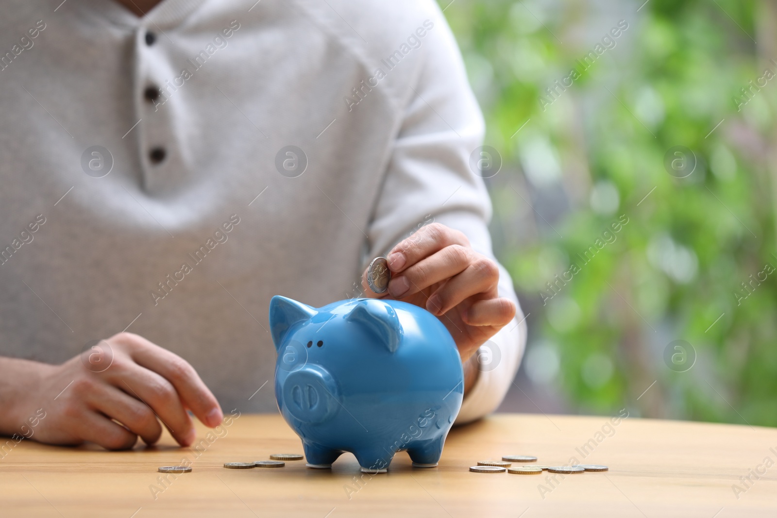 Photo of Man putting money into piggy bank at table, closeup