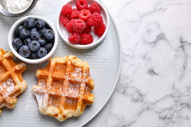 Photo of Delicious Belgian waffles with fresh berries and powdered sugar on white marble table, top view. Space for text