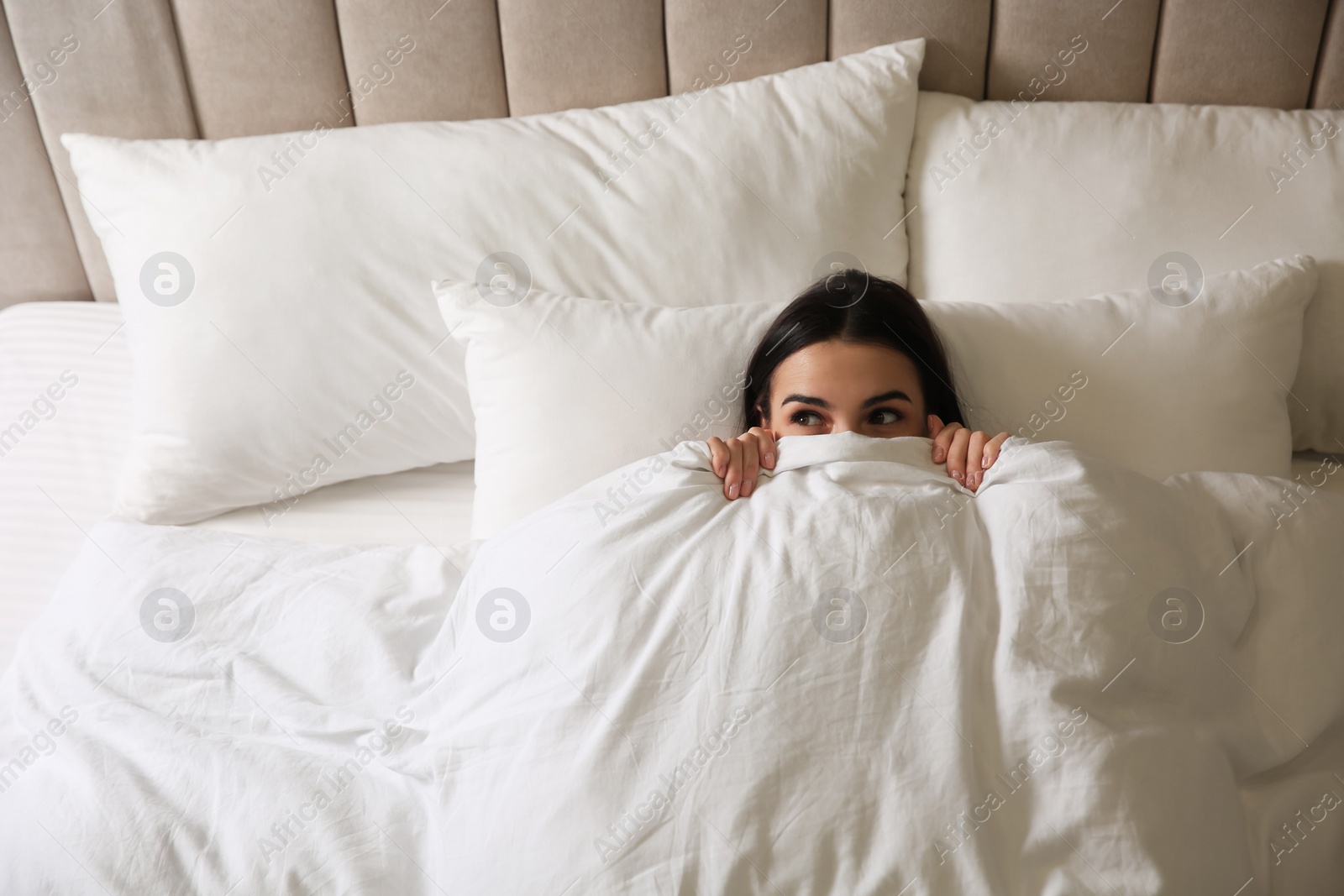 Photo of Young woman lying in bed covered with white blanket, top view