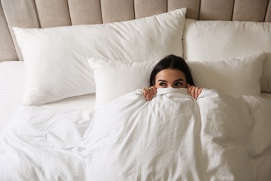 Young woman lying in bed covered with white blanket, top view