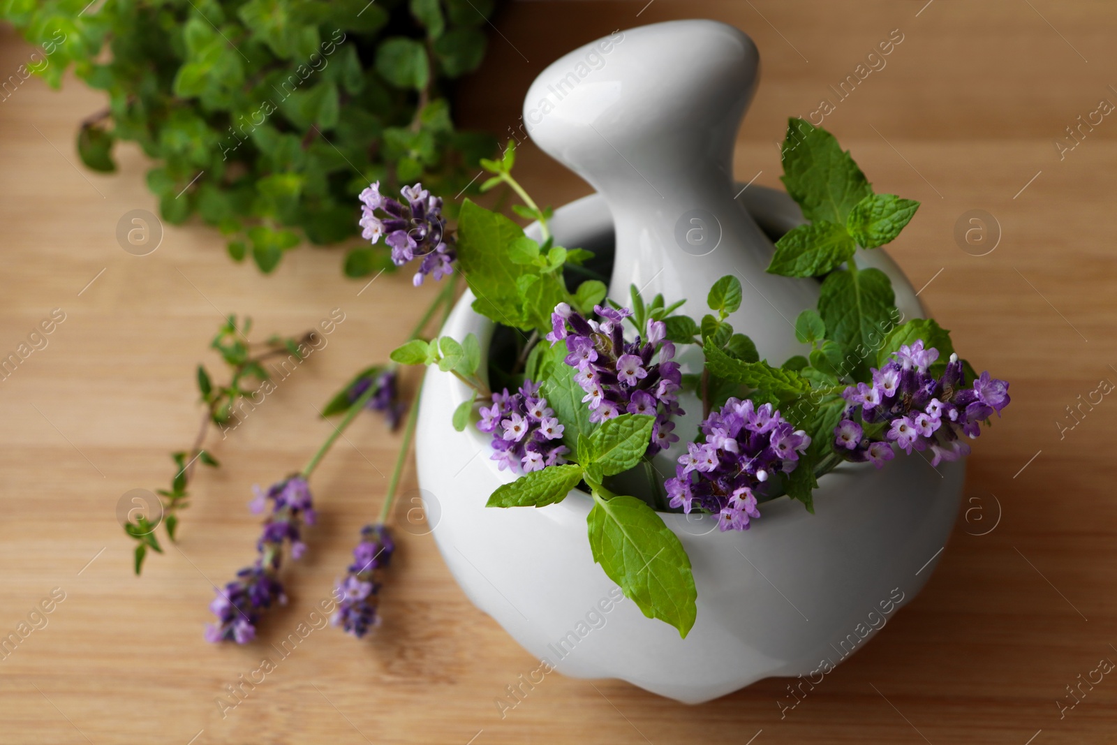 Photo of Mortar with fresh lavender flowers, mint and pestle on wooden table, closeup