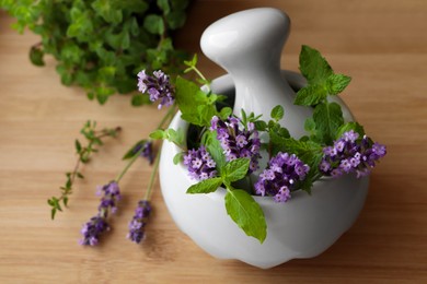 Photo of Mortar with fresh lavender flowers, mint and pestle on wooden table, closeup