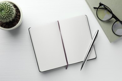 Photo of Open notebook, pen, glasses and cactus on white wooden table, flat lay. Space for text