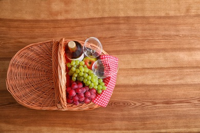 Picnic basket with wine, glasses and grapes on wooden table, top view. Space for text