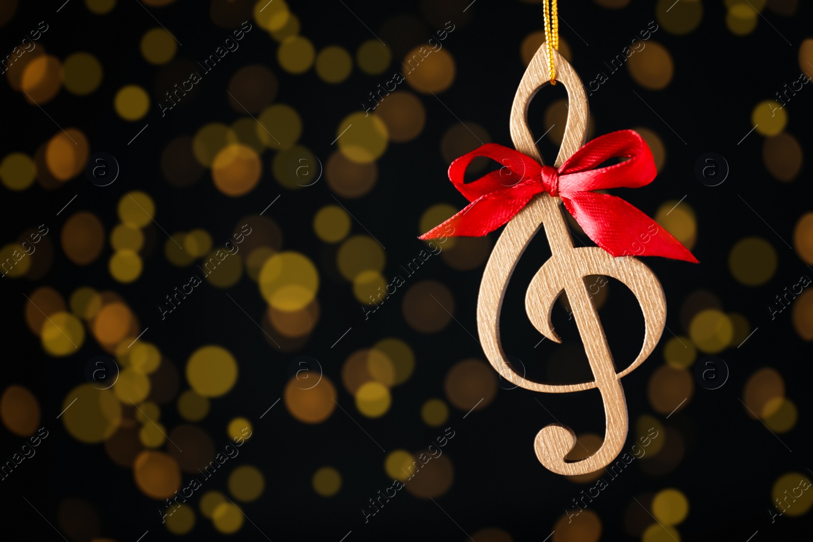 Photo of Wooden music note with red bow hanging on black background with blurred Christmas lights. Space for text