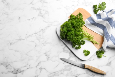 Fresh curly parsley, cutting board and knife on white marble table, flat lay. Space for text