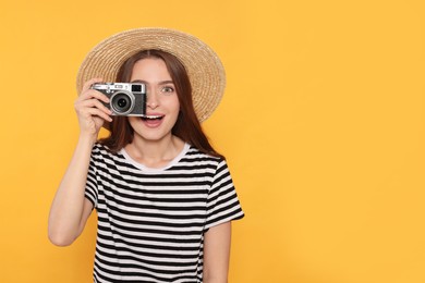 Young woman with camera taking photo on yellow background, space for text. Interesting hobby