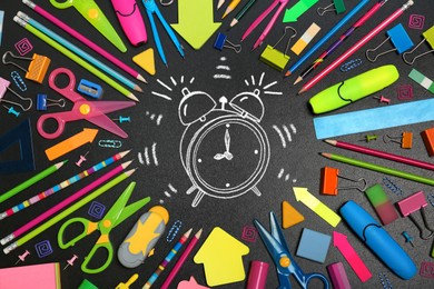 Image of Different stationery and drawn alarm clock on blackboard surface, flat lay. Time to school