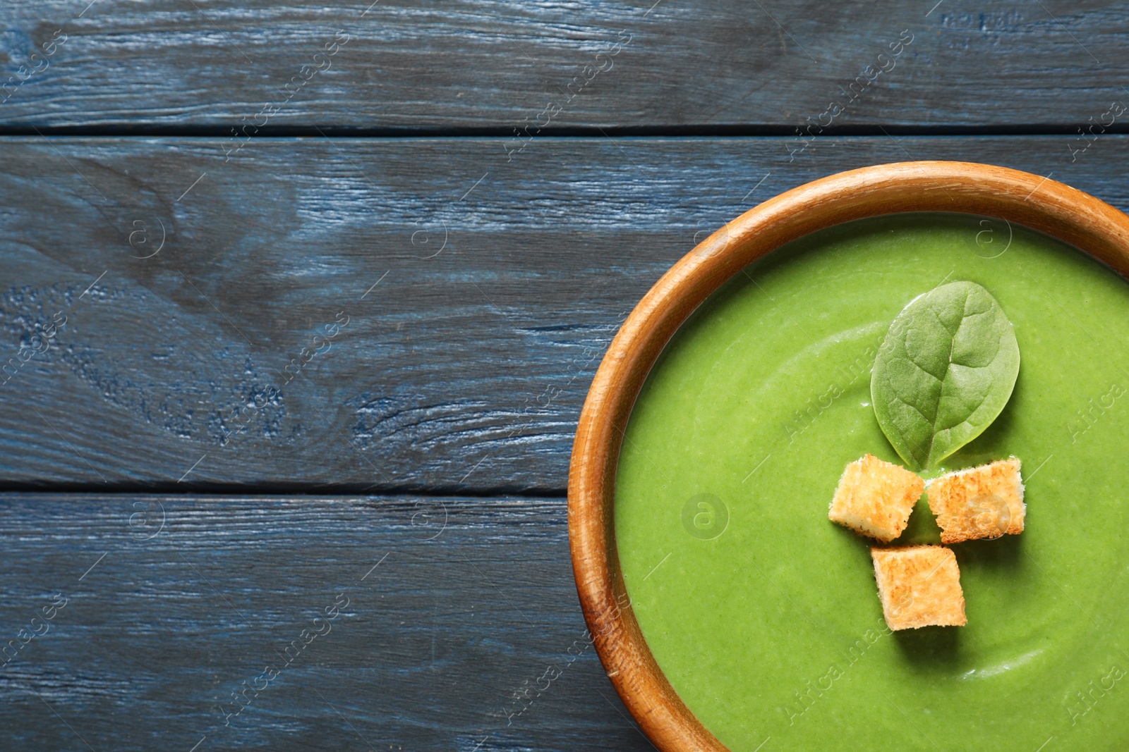 Photo of Fresh vegetable detox soup made of spinach with croutons in dish and space for text on wooden background, top view