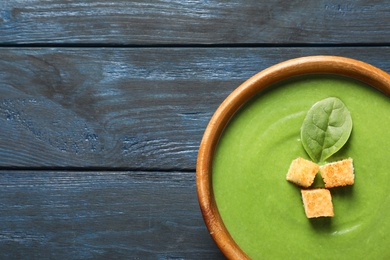 Fresh vegetable detox soup made of spinach with croutons in dish and space for text on wooden background, top view