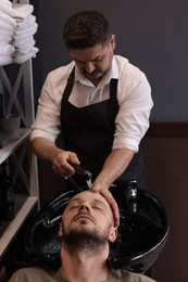 Professional hairdresser washing man's hair at sink in barbershop