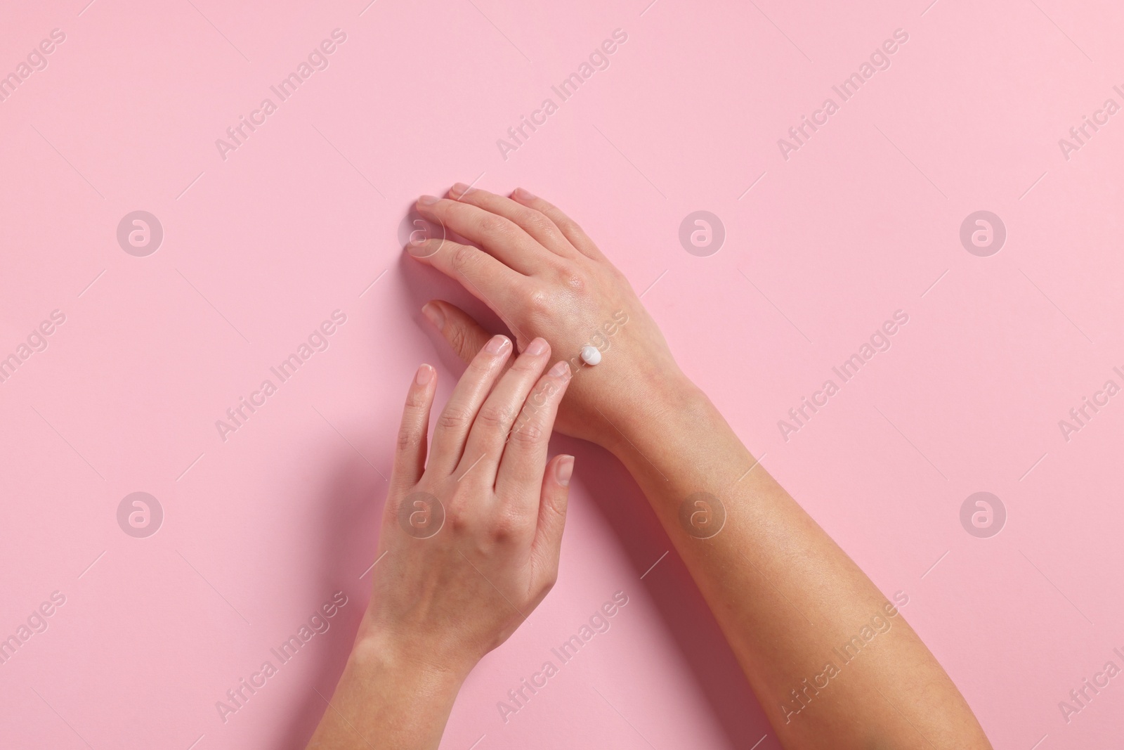 Photo of Woman applying cosmetic cream onto hand on pink background, top view