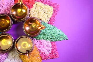 Photo of Diwali celebration. Diya lamps and colorful rangoli on purple background, flat lay