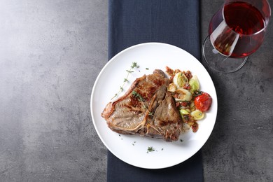 Photo of Delicious fried beef meat, vegetables and wine on grey table, top view. Space for text