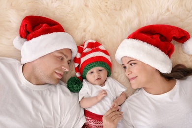 Photo of Happy couple with baby in Christmas hats on fuzzy rug, top view