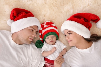 Happy couple with baby in Christmas hats on fuzzy rug, top view