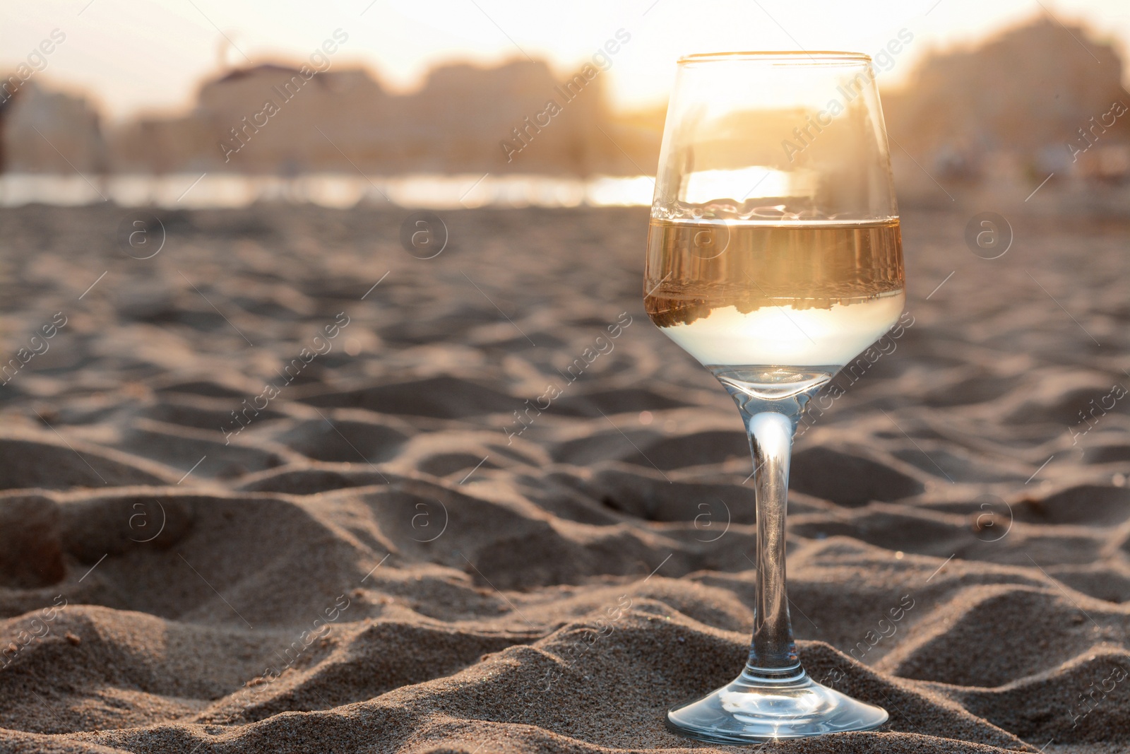 Photo of Glass of tasty wine on sandy beach, space for text