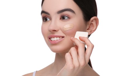 Photo of Teenage girl applying foundation on face with makeup sponge against white background