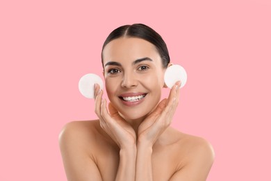 Beautiful woman holding cotton pads on pink background