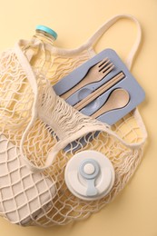 Photo of Fishnet bag with different items on beige background, top view. Conscious consumption