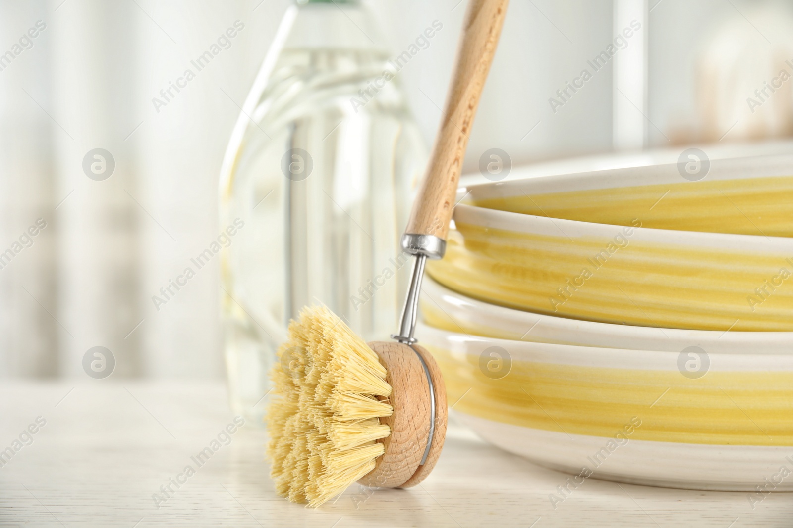 Photo of Cleaning brush for dish washing near bowls on white table indoors, closeup