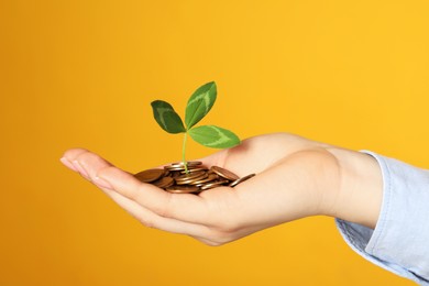 Photo of Woman holding coins with green sprout on yellow background, closeup. Investment concept