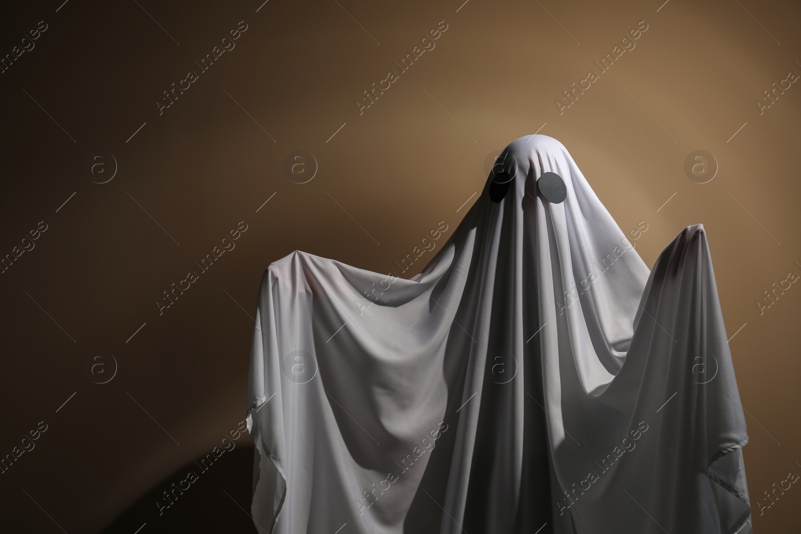 Photo of Creepy ghost. Woman covered with sheet on brown background, space for text