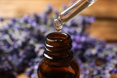 Photo of Dripping lavender essential oil into bottle, closeup