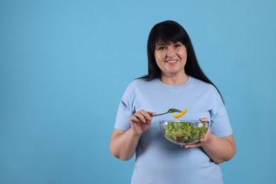 Photo of Beautiful overweight woman eating salad on light blue background, space for text. Healthy diet