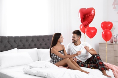 Photo of Young couple in bedroom decorated with air balloons. Celebration of Saint Valentine's Day