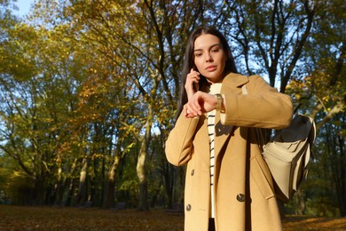 Photo of Woman checking time while talking on smartphone in park. Being late concept