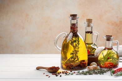 Cooking oil with different spices and herbs in jugs on white wooden table. Space for text
