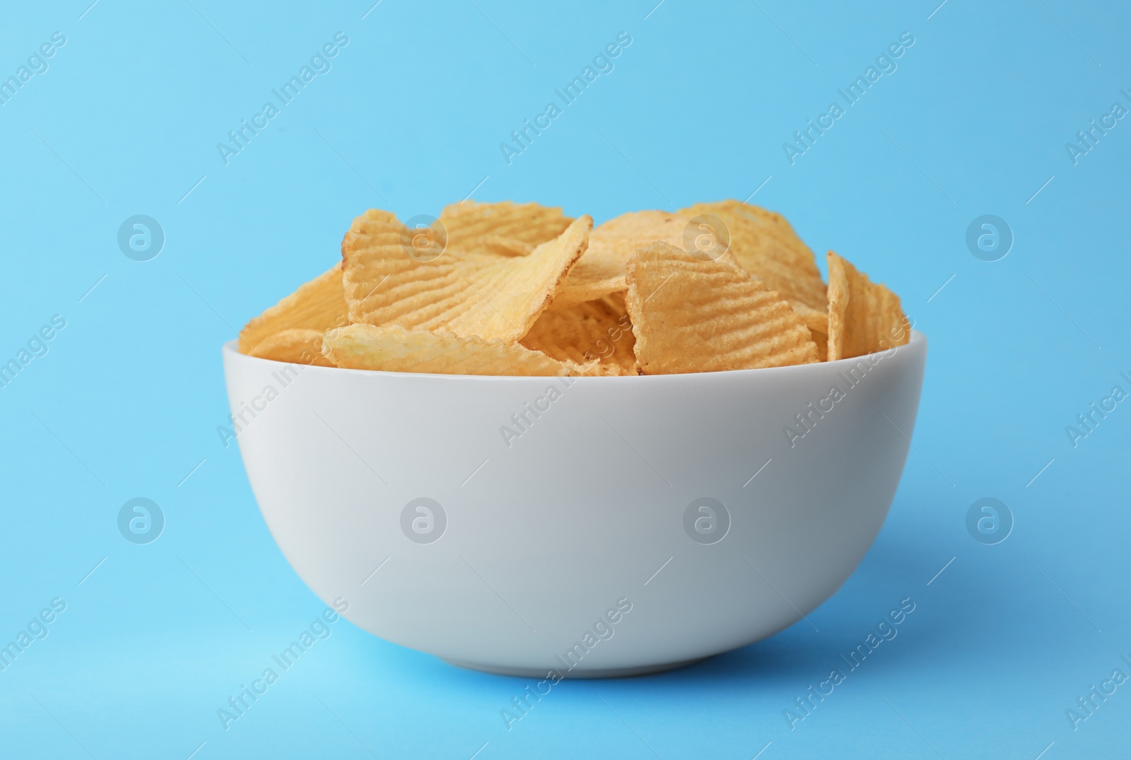 Photo of Delicious crispy potato chips in bowl on color background