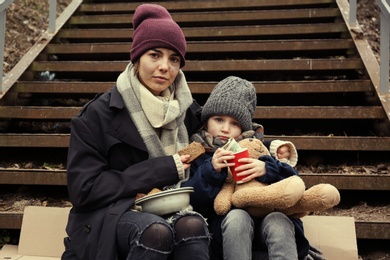 Photo of Poor mother and daughter with bread sitting on stairs outdoors
