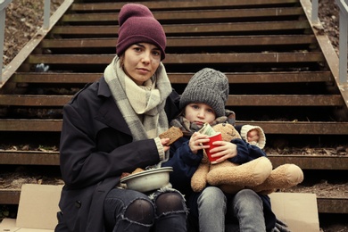 Poor mother and daughter with bread sitting on stairs outdoors