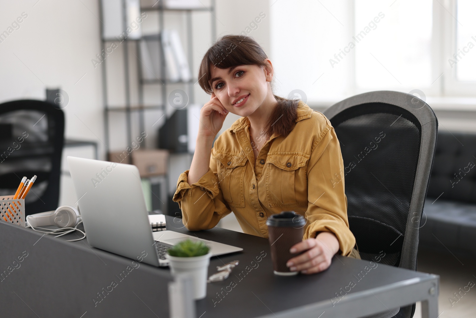 Photo of Woman with cup of coffee watching webinar at table in office