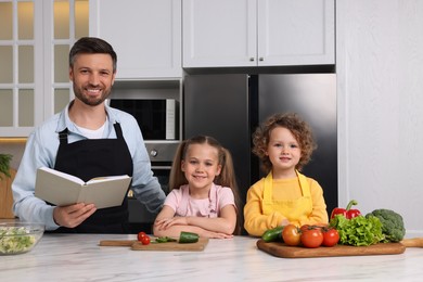 Photo of Happy man with his daughters cooking by recipe book in kitchen