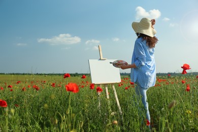 Photo of Woman painting on easel in beautiful poppy field