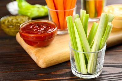 Photo of Celery sticks in glass bowl and dip sauce on wooden table
