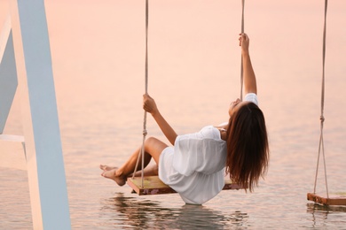 Photo of Young woman enjoying sunrise on swing over water