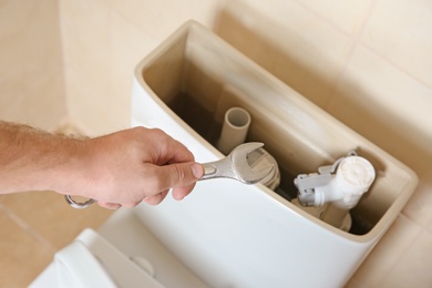 Photo of Plumber repairing toilet with wrench indoors, closeup