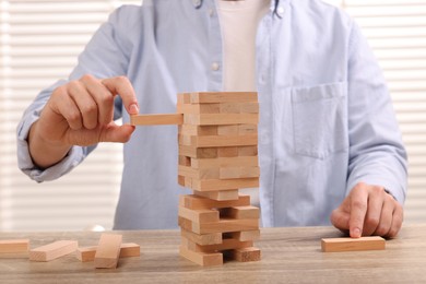 Photo of Playing Jenga. Man removing wooden block from tower at table, closeup