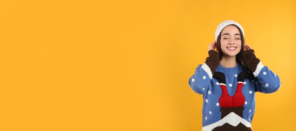 Young woman in Christmas sweater and hat on yellow background, space for text